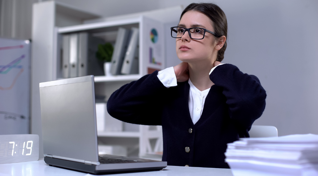 Ragazza al lavoro seduta su una scrivania che si tocca il collo per il dolore