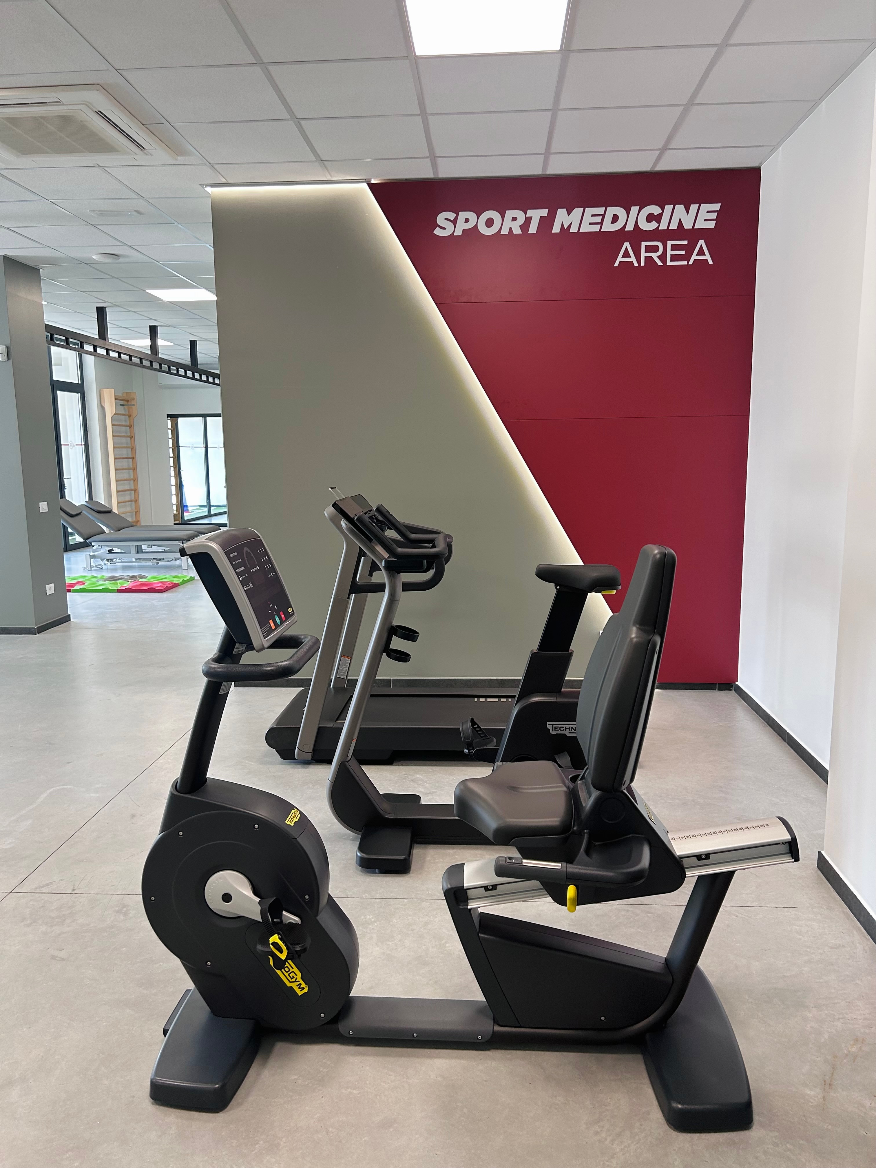 ingresso della nostra palestra CRR FisioFit: parete grigia e rossa con scritta Sport Medicine Area e davanti cyclette e tapis roulant