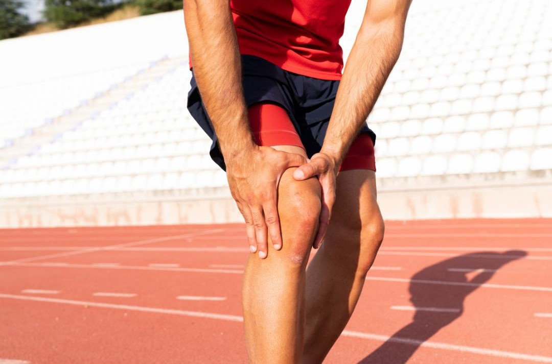 Atleta che si tocca il ginocchio dal dolore per infortunio sul campo d'atletica