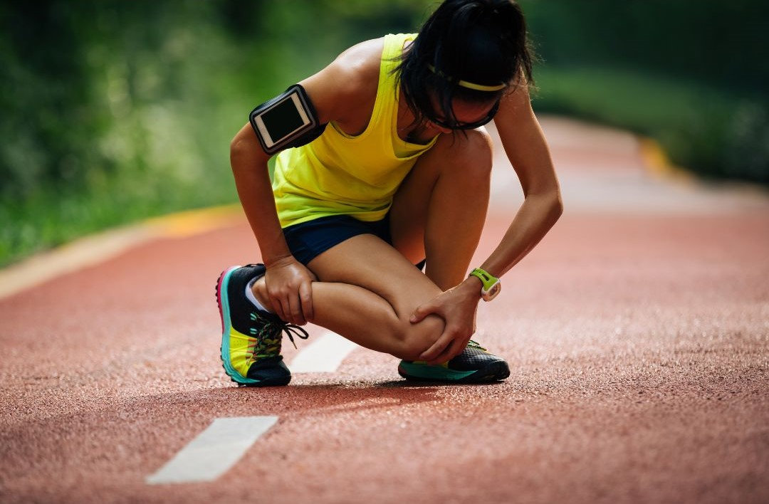 ragazza che si tocca la gamba in segno di infortunio, campo di atletica