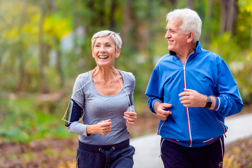 Due anziani che corrono all'aria aperta e sorridono